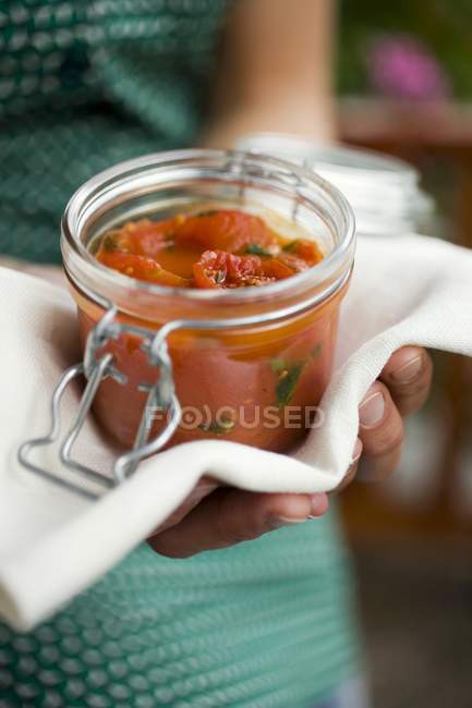 Mains tenant le pot de conservation de sauce tomate et tissu — Photo de stock