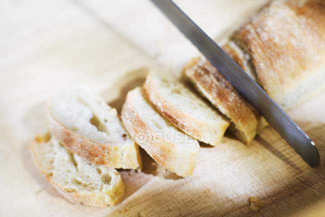 Slicing baguette with knife — Stock Photo