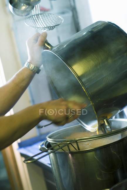 Hands emptying one pan into another in restaurant kitchen — Stock Photo