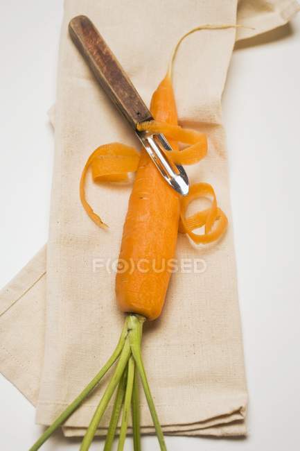 Pelar la zanahoria con pelador de verduras - foto de stock