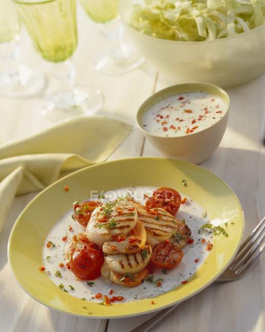 Жареные гребешки с помидорами на желтой тарелке за столом — стоковое фото