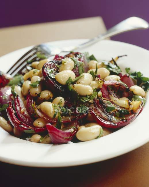 Bean salad with grilled onions on white plate with fork — Stock Photo