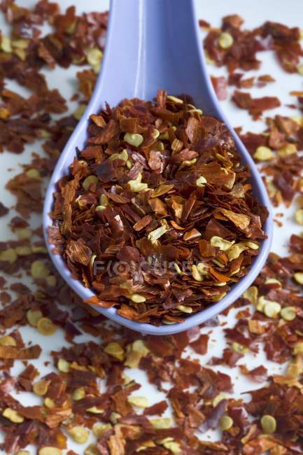 Dried chilli flakes with blue spoon over white surface — Stock Photo