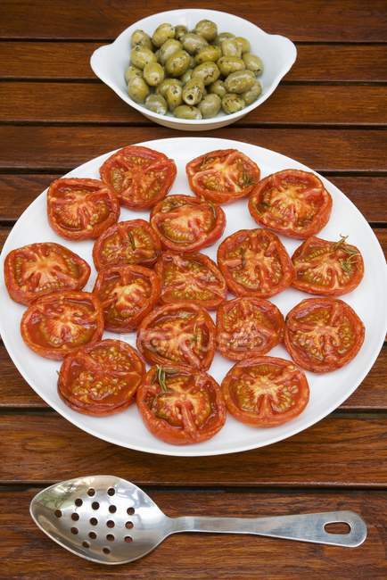 Fried tomatoes and pickled olives  on white plate over wooden surface — Stock Photo