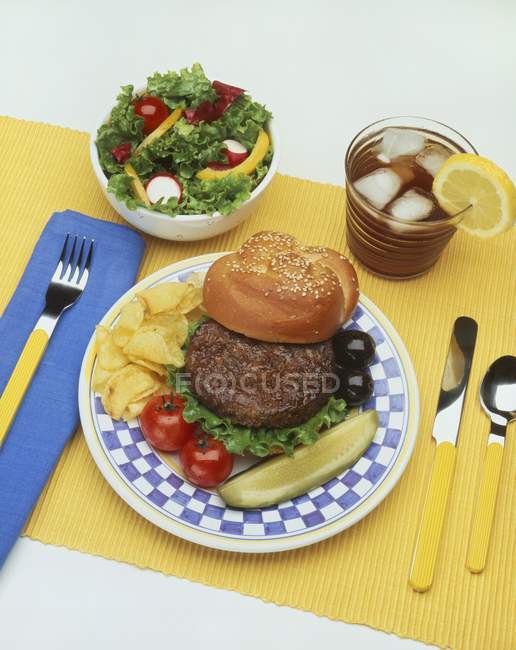 Closeup view of hamburger with pickle, chips, salad and iced tea — Stock Photo