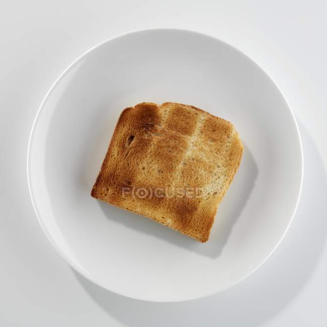 Primer plano vista superior de una rebanada de pan tostado en un plato blanco - foto de stock