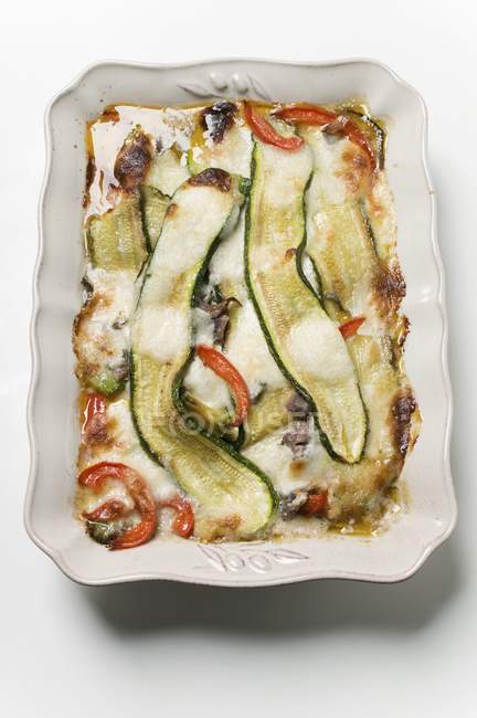 Pepper and courgette gratin on white plate over white surface — Stock Photo