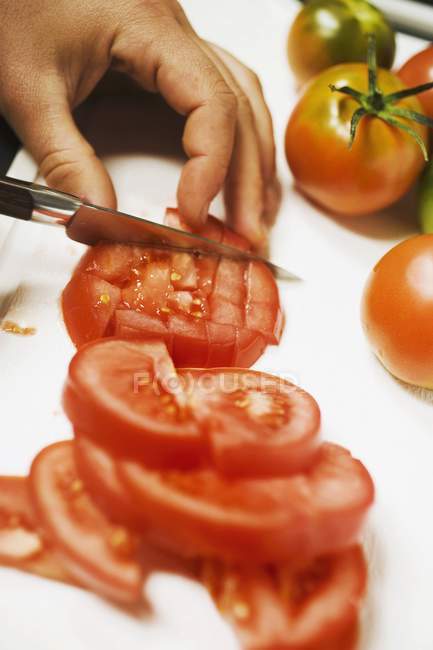 Tagliare a dadini il pomodoro sulla scrivania bianca con un coltello in mano — Foto stock
