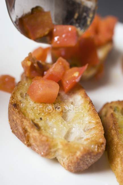 Putting diced tomatoes on toasted baguette slice — Stock Photo
