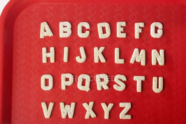 Vista de primer plano de las galletas de azúcar alfabeto en bandeja de plástico rojo - foto de stock