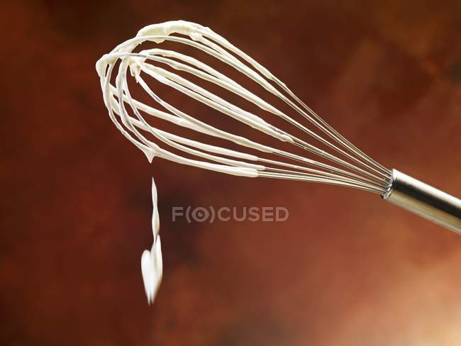 Closeup view of a whisk with dripping whipped cream — Stock Photo
