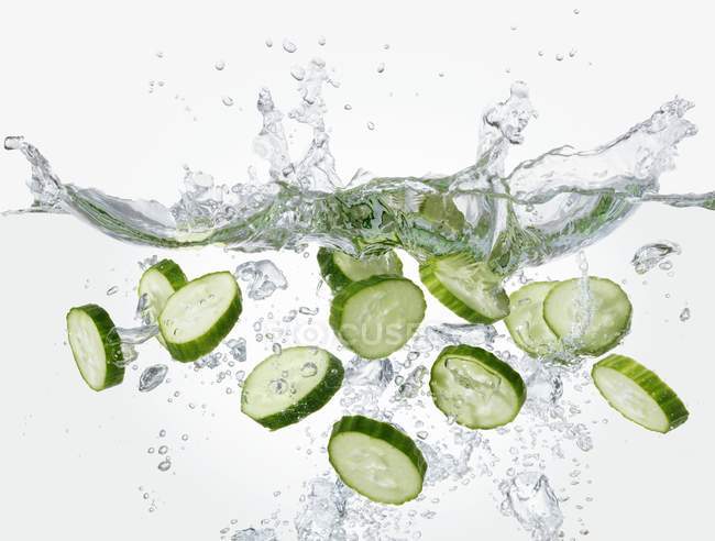 Slices of cucumber falling into water — Stock Photo