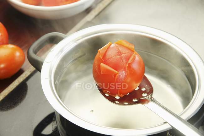 Blanching tomatoes in metal pot with spoon — Stock Photo