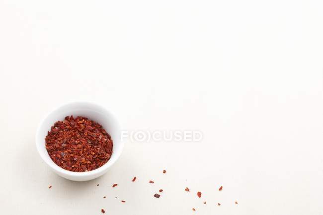 Vista elevada de flocos de pimenta em uma tigela e na superfície branca — Fotografia de Stock