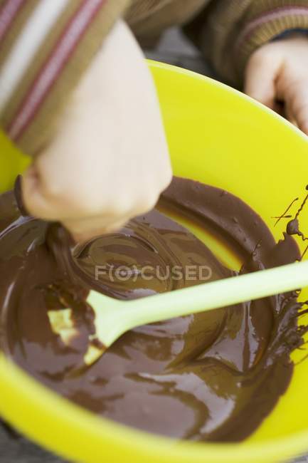 Closeup view of child hand reaching in chocolate mixture in yellow bowl — Stock Photo