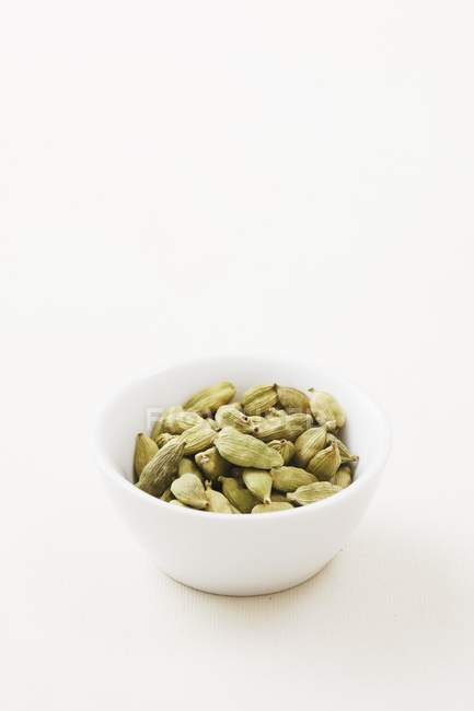 Elevated view of a bowl of cardamon capsules on white surface — Stock Photo