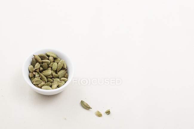 Elevated view of cadamom capsules in a bowl and on white surface — Stock Photo