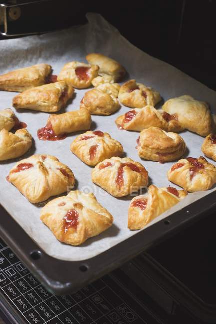 Closeup view of baked puff pastries with berry filling on baking tray in oven — Stock Photo