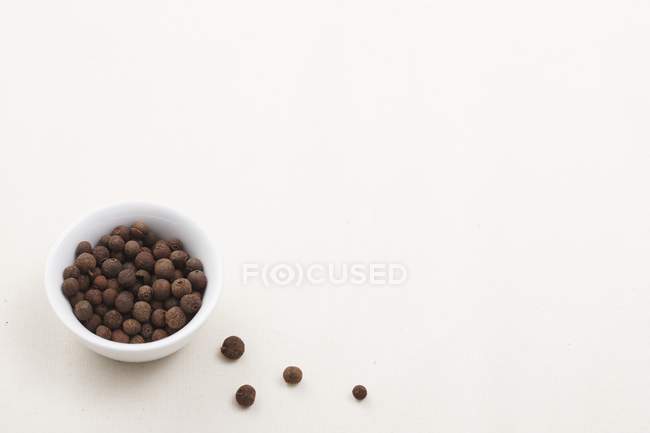 Closeup view of allspice berries in a bowl and on white surface — Stock Photo