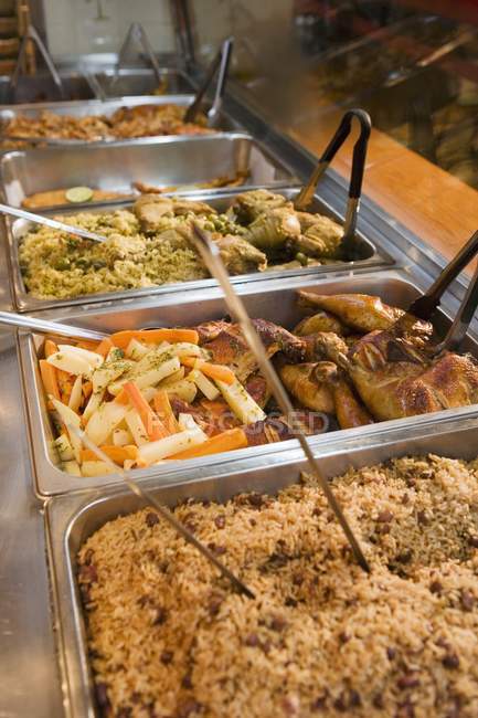 Vista elevada de los alimentos españoles calientes en bandejas buffet con cucharas y pinzas - foto de stock