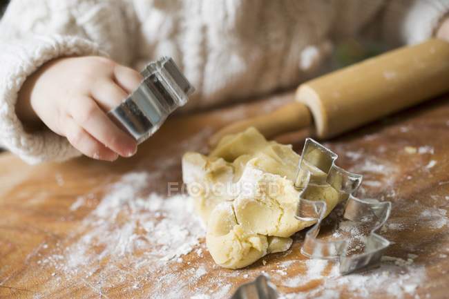 Cropped view of child holding cookie cutter over biscuit dough — Stock Photo