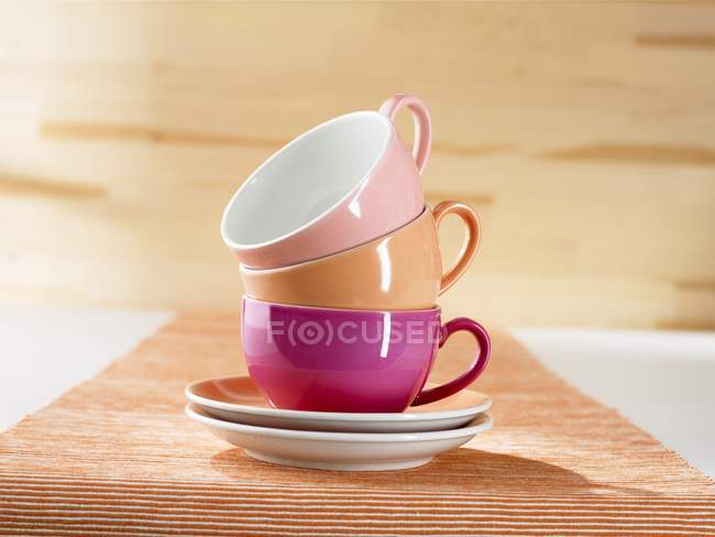 Closeup view of a stack of colorful cups and saucers on striped cloth — Stock Photo