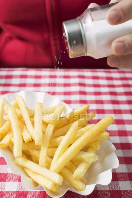 Mão salpicando sal em batatas fritas — Fotografia de Stock