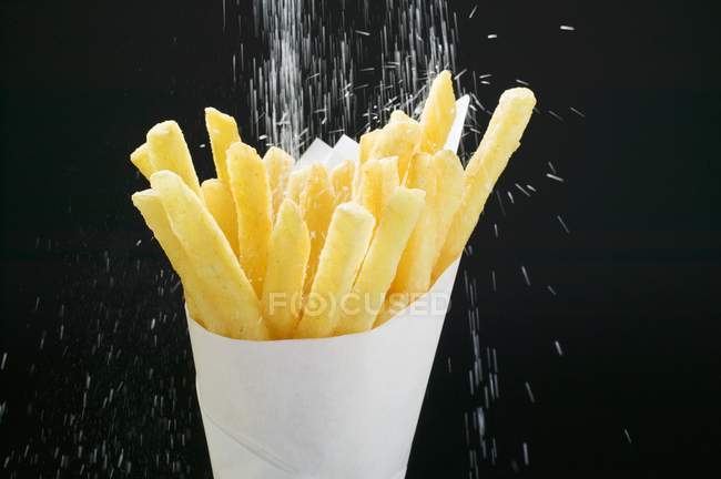 Espolvorear sal sobre papas fritas - foto de stock