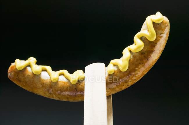 Sausage with mustard in wooden tongs — Stock Photo