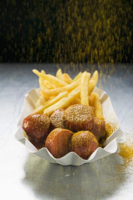 Pó de caril de aspersão em currywurst e batatas fritas — Fotografia de Stock