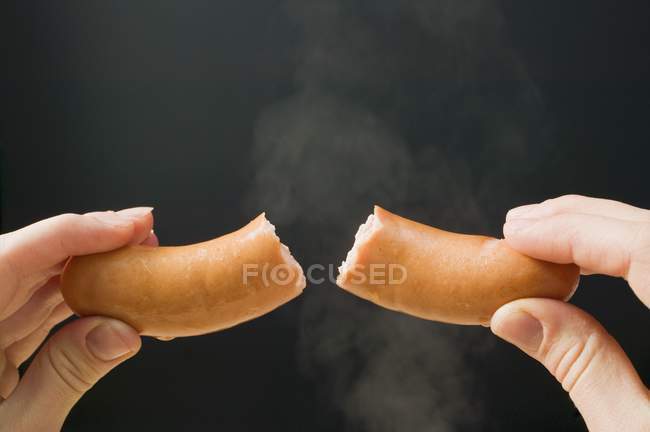 Mão segurando um frankfurter reduzido para metade — Fotografia de Stock