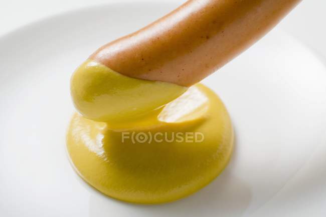 Dipping frankfurter in mustard — Stock Photo