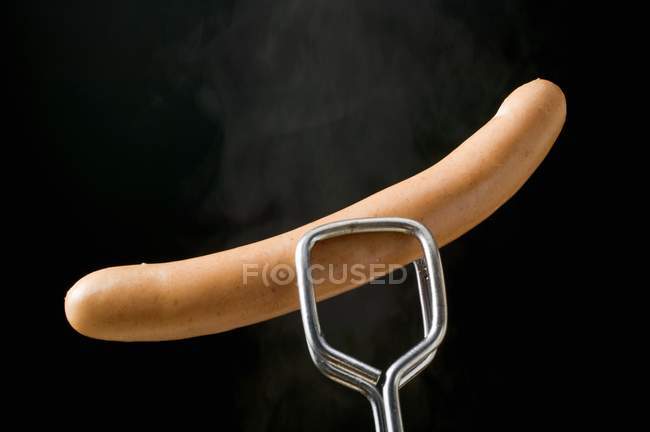 Tongs holding frankfurter — Stock Photo
