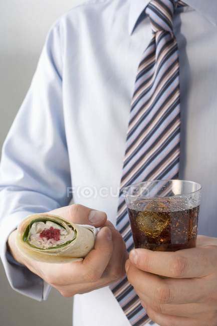 Крупный план человека в рубашке и галстуке, держащего съедобную обертку и колу — стоковое фото