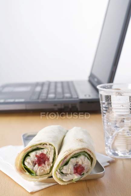 Closeup view of tuna wraps and mineral water in front of laptop — Stock Photo