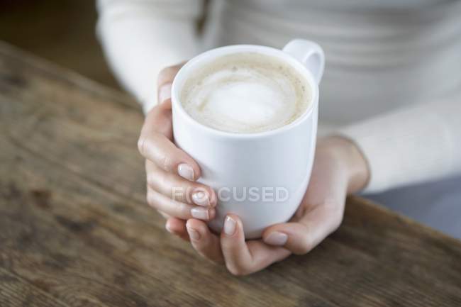 Vista close-up de mãos segurando um copo Cappuccino — Fotografia de Stock