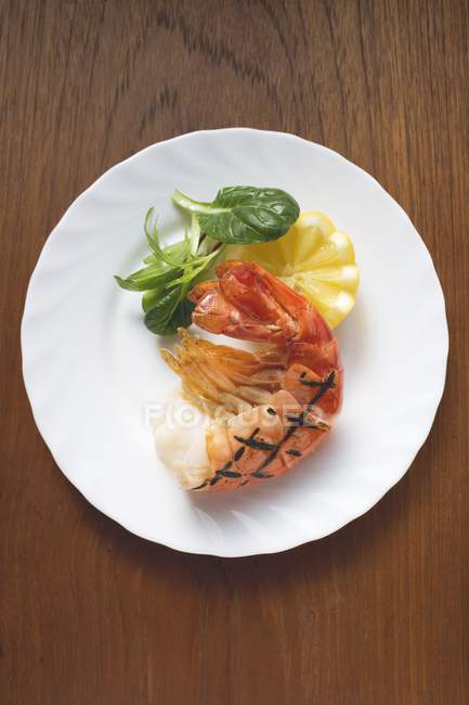 Vista dall'alto di gamberetti alla griglia con insalata di mais e limone su piatto bianco — Foto stock