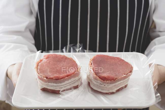 Chef sosteniendo carne de res envuelta en tocino - foto de stock