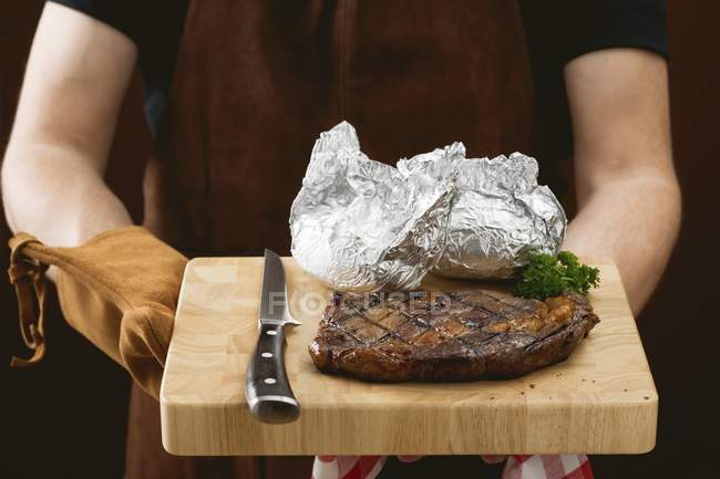 Человек держит стейк с запечённой картошкой — стоковое фото