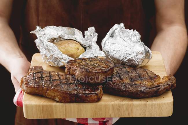 Man holding steaks with baked potatoes — Stock Photo