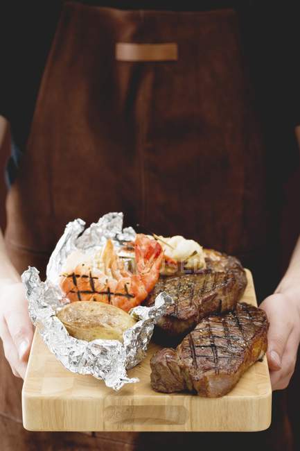 Hombre sosteniendo filetes con papas al horno - foto de stock