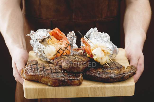 Hombre sosteniendo filetes con papas al horno - foto de stock
