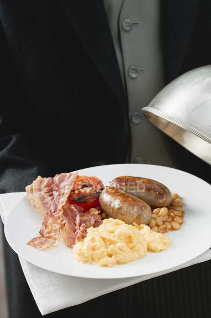 Butler serving English breakfast on plate with dome cover — Stock Photo