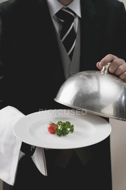 Butler serving tomato and parsley on plate with dome cover, midsection — Stock Photo
