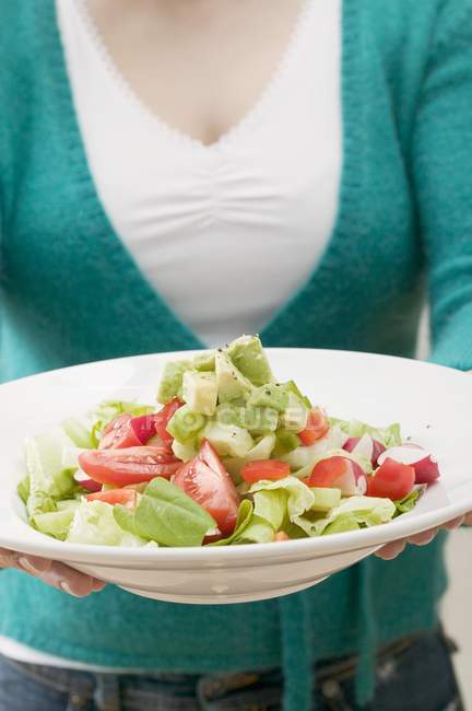 Женщина держит тарелку салата с авокадо и помидорами в руках, в середине — стоковое фото