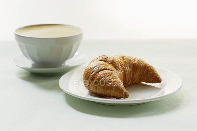 Milchkaffee mit Croissant auf Teller — Stockfoto