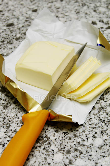 Vista de primer plano de la mantequilla en rodajas con cuchillo en el envoltorio - foto de stock