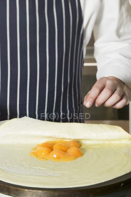 Closeup cropped view of person folding crepe with apricot filling — Stock Photo