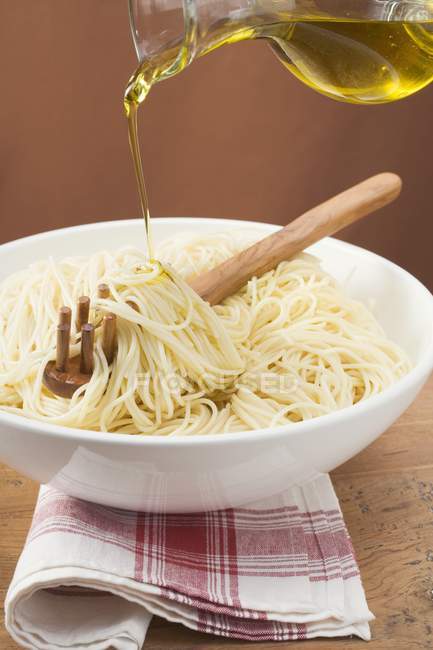 Verter aceite de oliva sobre espaguetis cocidos - foto de stock