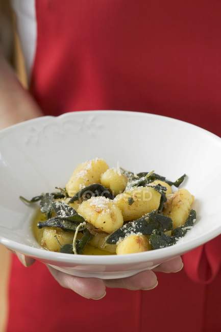 Closeup cropped view of hand holding plate of Gnocchi in sage butter — Stock Photo